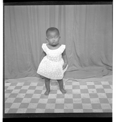 Full frontal view of a little girl standing in the studio wearing a dress.From Endangered Archives Programme EAP449, "Social history and cultural heritage of Mali"