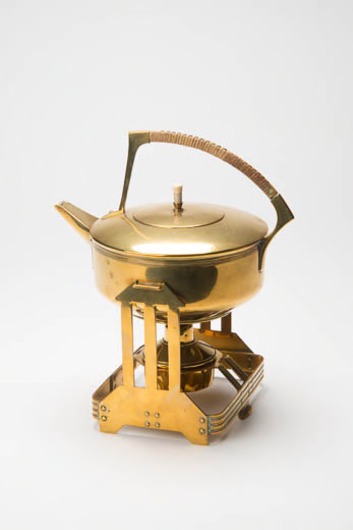 Geel koperen ketel met rieten handvat op bijpassend komfoor met brander
