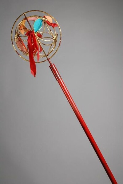 Dresseerbol of 'dancing ball', lange rode stok met een open goudkleurige metalen bol met veelkleurige stukjes stof, onderdeel van het danskostuum voor de drakendans